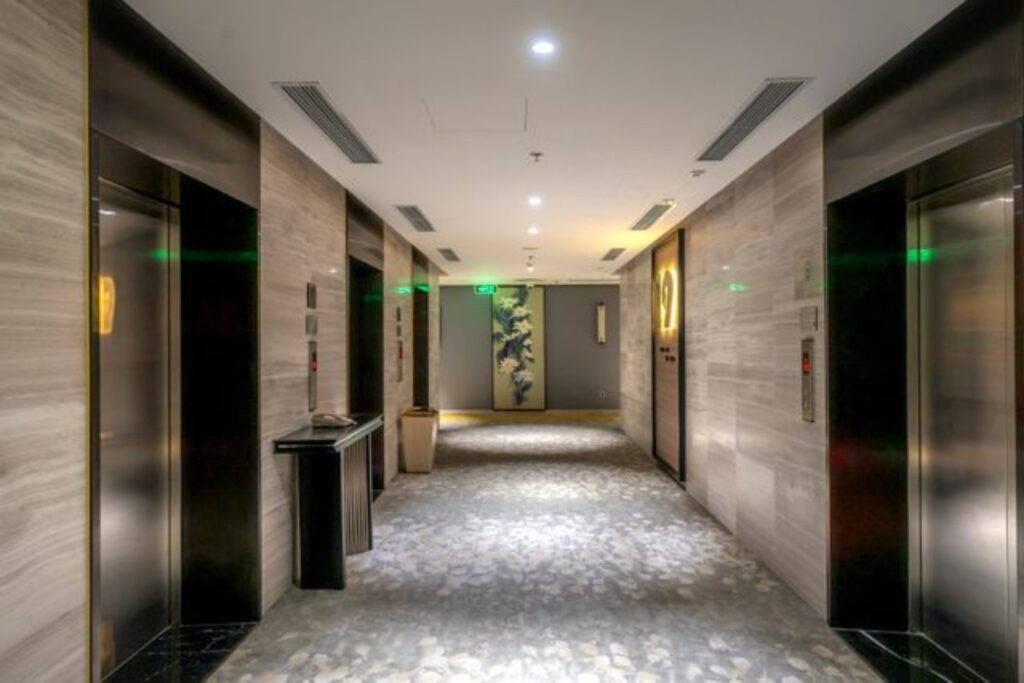 Modern apartment building lift lobby with multiple elevators, stone walls and carpeted flooring
