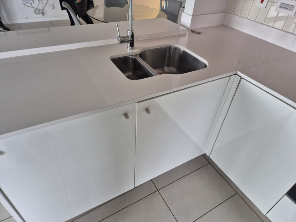 Modern kitchen after professional cleaning with polished worktops, stainless-steel sink and white cabinetry