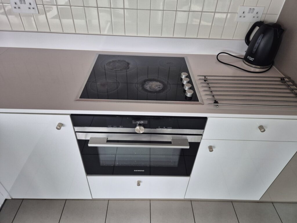 Modern kitchen cooking area after professional cleaning with induction hob, built-in oven, worktop and white cabinetry