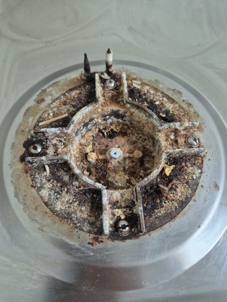 Heavily soiled gas hob burner base with burnt-on grease, food residue and grime