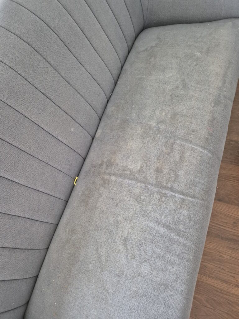 Heavily soiled grey fabric sofa seat with visible staining and embedded dirt before professional upholstery cleaning