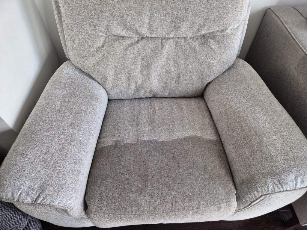 Grey upholstered armchair during professional upholstery cleaning, showing one half cleaned and the other half heavily soiled