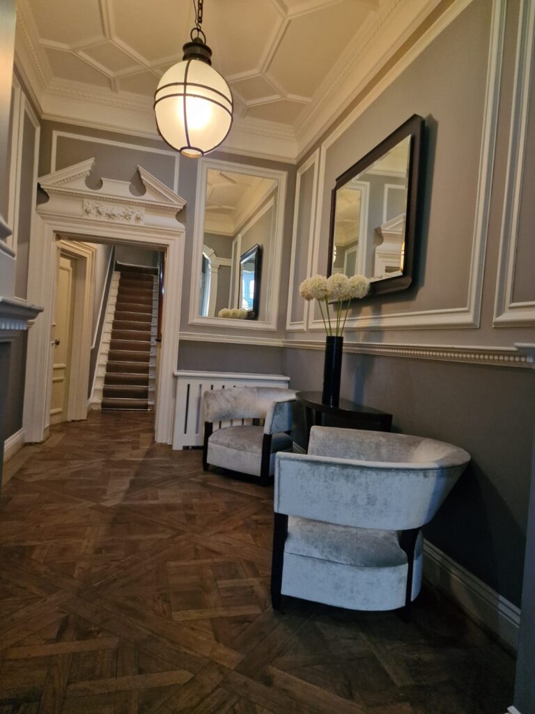 Elegant hallway after professional cleaning with parquet flooring, upholstered chairs, mirrors and decorative wall paneling