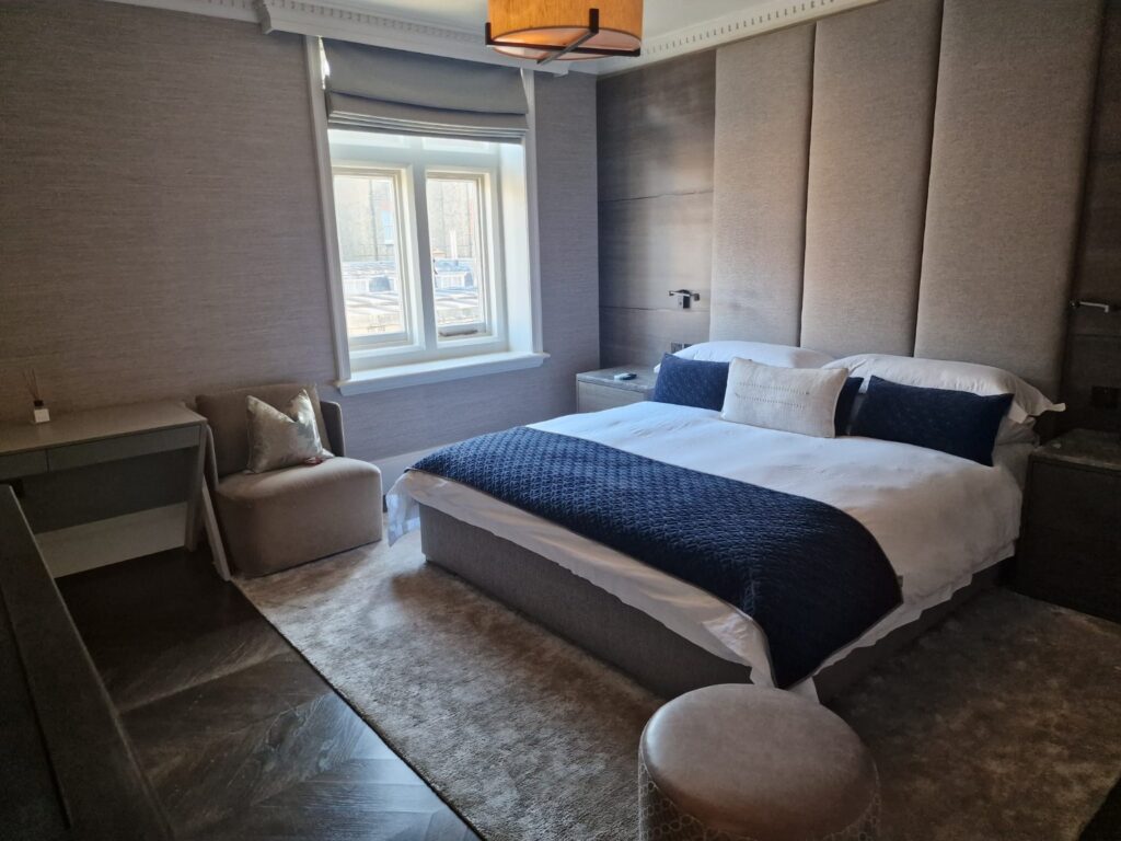 Modern bedroom with upholstered bed, armchair, fitted wall panels and carpeted flooring