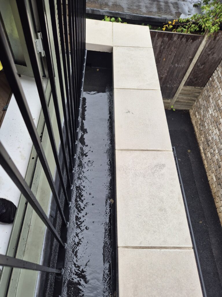 Balcony gutter after jet washing, cleared of debris and algae with a much cleaner surface
