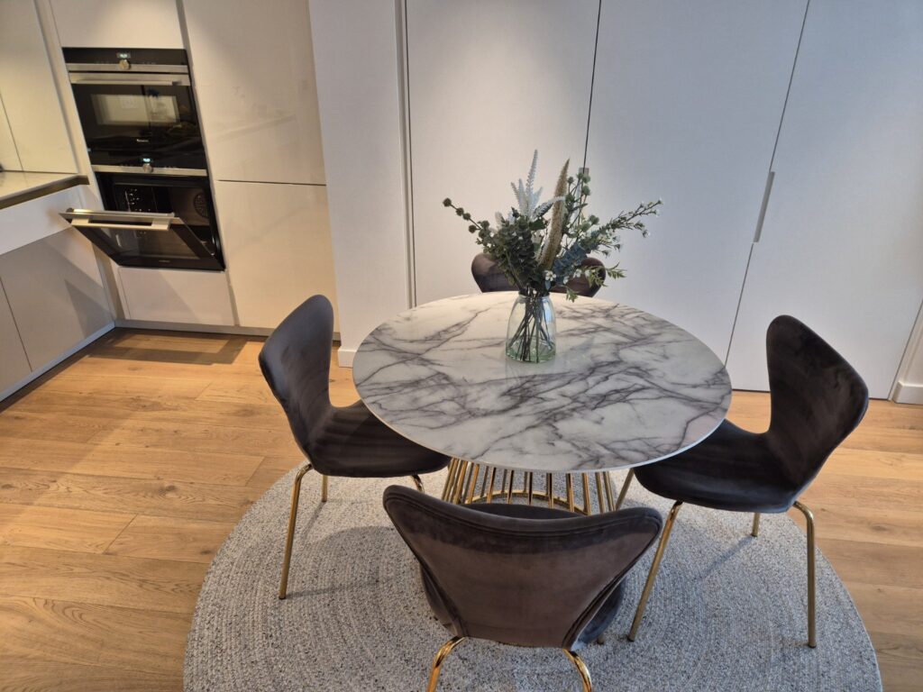Modern dining area after professional cleaning with marble table, upholstered chairs and fitted kitchen