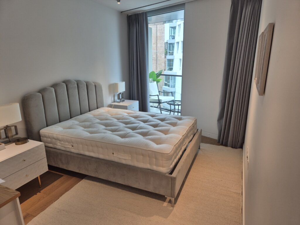Modern bedroom after professional cleaning with upholstered bed, bedside tables, carpet and balcony access